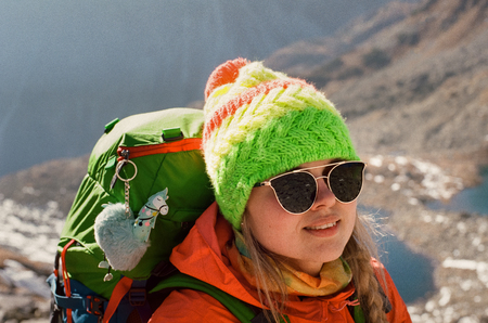 Closeup portrait of happy blonde backpacker in sunglasses and colorful outfit posing on mountain lake background on a sunny day in Slovakia. SShot with film camera and grainの写真素材