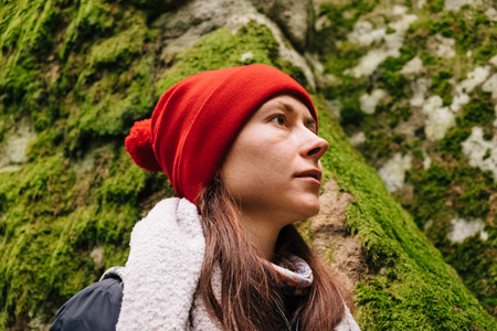 Closeup portrait of young caucasian female with long brown hair on the stone wall covered with green moss background in the forest somewhere in Carpathians, in Autumn. Low angle view.の写真素材