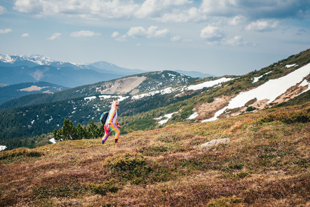 Full-length portrait of a female backpacker in a unicorn suit walking across Carpathian mountains covered with snow leftovers on a sunny Spring day. Wanderlust travel concept.の写真素材