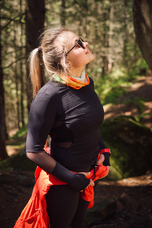 Young smiling blonde hiker in sunglasses posing in forest on a sunny Spring day. Concept of tourism.の写真素材