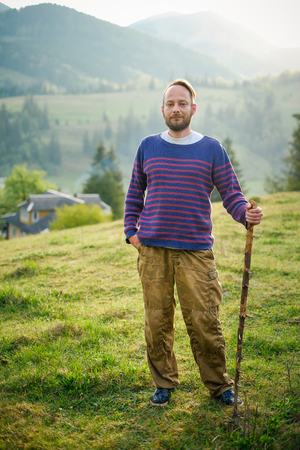 Handsome man traveling with a wooden stick on the morning mountain at sunrise. Wanderlust concept.の写真素材