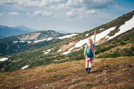 Full-length portrait shot from back of a female backpacker in a unicorn suit celebrating success on a Carpathian mountains background covered with snow leftovers on a Spring day. Wanderlust concept.の写真素材