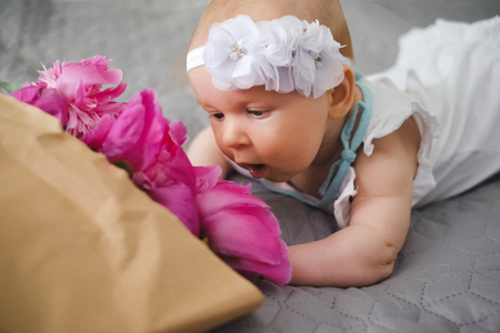 Cute newborn baby lying on the bed and playing with ping bouquet of pion flowersの写真素材