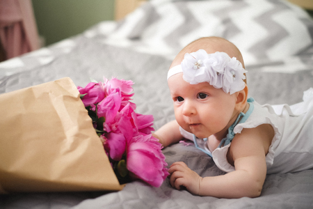 Newborn baby lying on the bed and playing with ping bouquet of pion flowersの写真素材