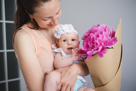 Happy young mother hugging her newborn child and help explore the world showing flowers bouquetの写真素材