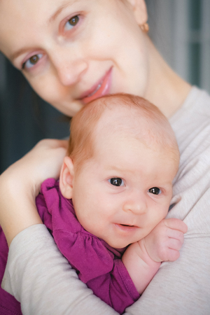 Portrait of happy young mother hugging and kissing her sweet adorable newborn childの写真素材