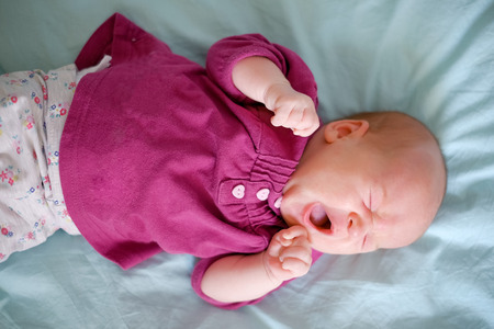 Newborn baby lying on the bed and sweet yawnの写真素材