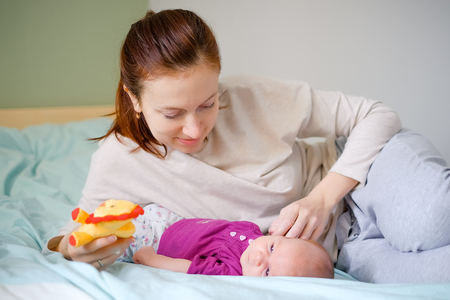 Newborn baby playing with mother on the bed. Tenderness and love emotions of happy familyの写真素材
