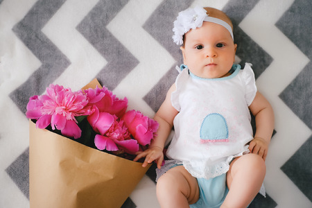 Newborn baby lying on the bed and playing with ping bouquet of pion flowersの写真素材