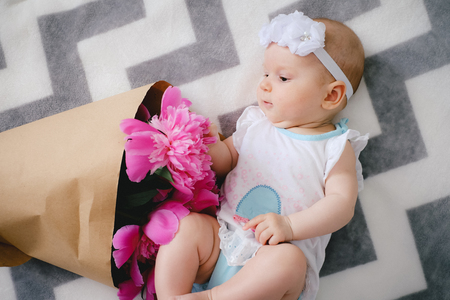 Newborn baby lying on the bed and playing with ping bouquet of pion flowersの写真素材