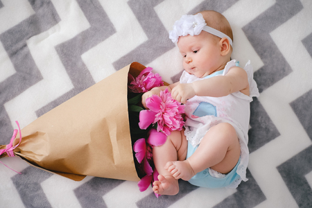 Newborn baby lying on the bed and playing with ping bouquet of pion flowersの写真素材