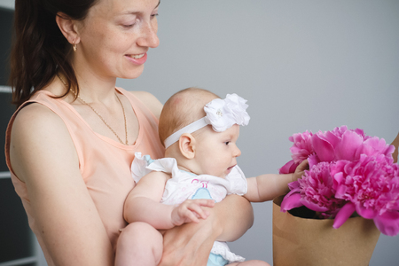 Portrait of happy young mother with flowers bouquet hugging her newborn childの写真素材