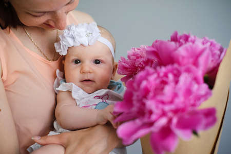 Happy young mother hugging her newborn child and help explore the world showing flowers bouquetの写真素材