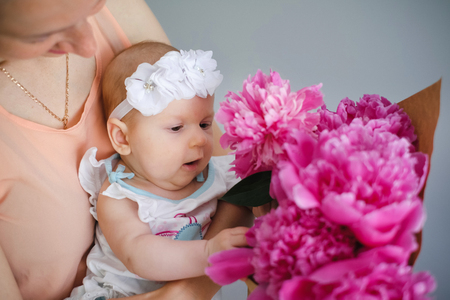Happy young mother hugging her newborn child and help explore the world showing flowers bouquetの写真素材