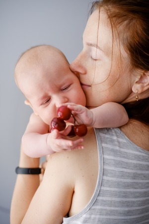 Tenderness and love. Newborn baby with mother explore the world and try fruitsの写真素材