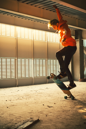 Extreme street sport. Hipster man jumping and riding on long board at an abandoned building at sunset. Image with grainの写真素材