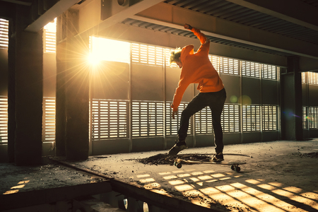 Extreme street sport. Hipster man jumping and riding on long board at an abandoned building at sunset. Image with grainの写真素材