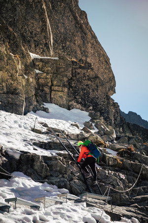 Female hiker climbing up on ladder to the mountain top in winter. Rysy. Slovakia.の写真素材
