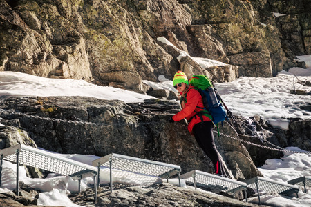 Female hiker climbing up on ladder to the mountain top in winter. Rysy. Slovakia.の写真素材