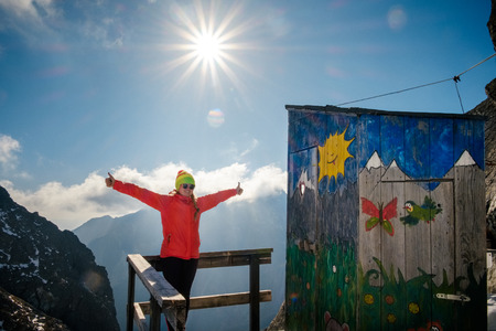 Poprad, Slovakia - October 2, 2017: Woman hiker happy with raised up hands near unique mountain altitude toilet. Travel destination scenes in High tatras mountain in Slovakiaのeditorial素材