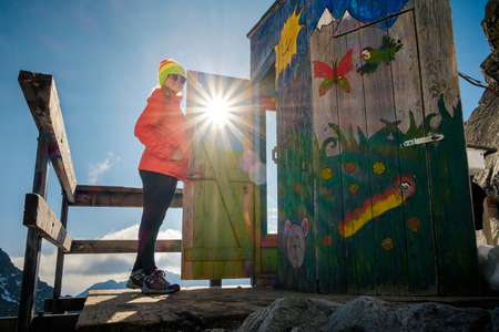 Poprad, Slovakia - October 2, 2017: Woman hiker happy landscape near unique mountain altitude toilet. Travel destination scenes in High tatras mountain in Slovakiaのeditorial素材