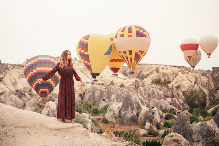 Beautiful woman enjoying amazing view and walking in Cappadocia landscape with hot air balloon on  at sunrise. Travel in Turkeyの写真素材