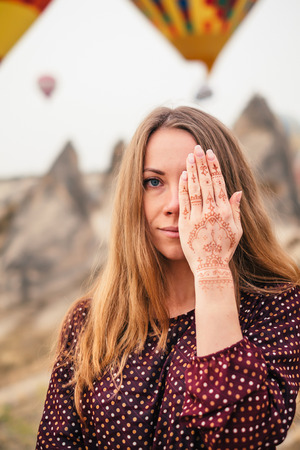 Portrait of a beautiful girl in colorful scarf covering one eye with a hand that has a mehendi tattoo. Looking at camera.の写真素材
