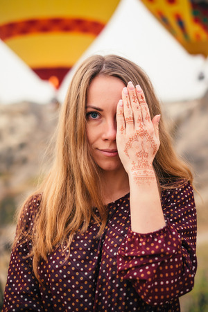 Closeup woman portrait with beautiful eyes and mehendi henna tattoo on hand in Cappadocia landscape and hot air balloonの写真素材