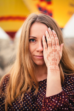 Portrait of a beautiful girl in colorful scarf covering one eye with a hand that has a mehendi tattoo. Looking at camera.の写真素材