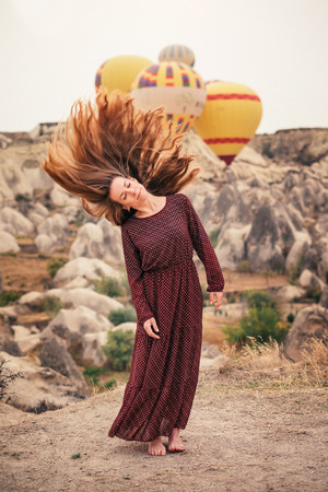 Beautiful woman enjoying and waving hair in Cappadocia landscape with hot air balloonの写真素材