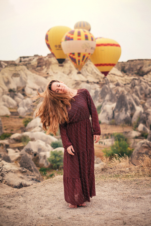 Beautiful woman enjoying and waving hair in Cappadocia landscape with hot air balloonの写真素材