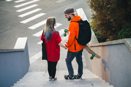 Hipster couple holding hands and walking on the city street after riding on skateboard at sunset timeの写真素材