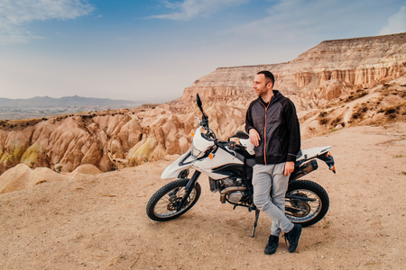 Handsome man riding and explore Cappadocia mountain valley landscape on enduro motorcycle at sunset. Travel to Turkeyの写真素材