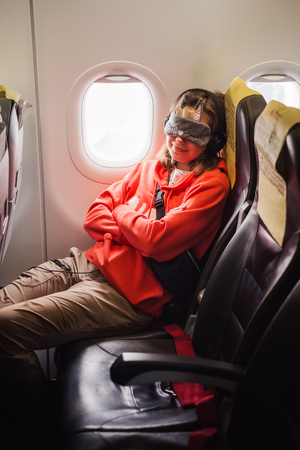 Tourist woman passenger fly in airplane and sleep in eyes mask near the windowの写真素材