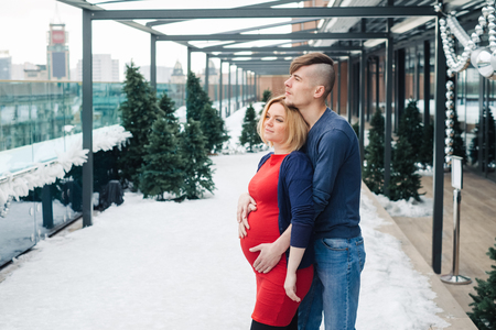 Family with pregnant woman siting on the roof top of the skyscraper in winter city back. Young wife with husband enjoy spend time togetherの写真素材