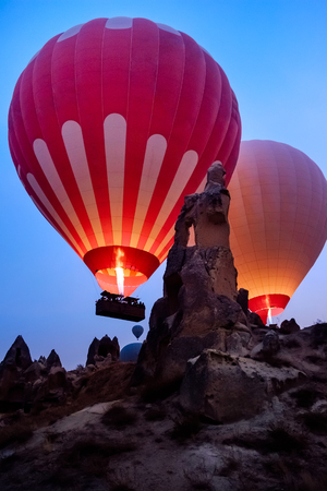 Colorful hot air balloons flying over beautiful Goreme landscape at night on blue sky before sunrise. Cappadocia mountains, Turkey. High ISO image with grainの写真素材