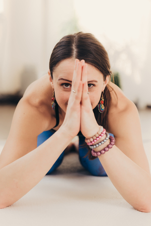 Portrait of beautiful young woman meditating and doing namaste hand gesture on a sunny morning at studio.の写真素材