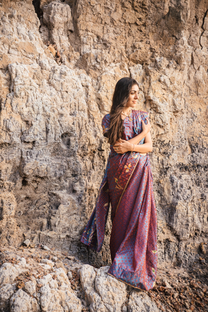 Fashion shoot of indian woman in traditional clothes. Woman in beautiful saree standing on the rock near the beachの写真素材