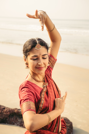 Indian classical dance Bharatanatyam performed by beautiful woman in traditional clothes at sunsetの写真素材
