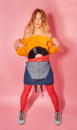 Funny retro styled fashionable woman holding vintage vinyl record on pink background. Fashion back to 80s - 90s new trend conceptの写真素材