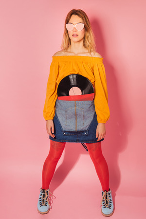 Funny retro styled fashionable woman holding vintage vinyl record on pink background. Fashion back to 80s - 90s new trend conceptの写真素材