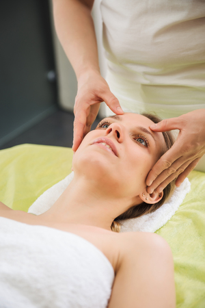 Beautiful woman relaxing and enjoying a head massage in a spa centerの写真素材