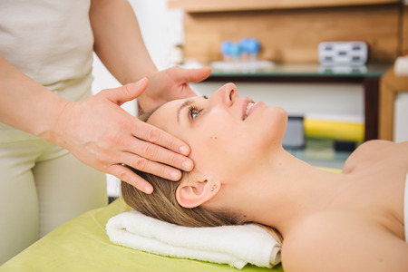 Beautiful woman relaxing and enjoying a head massage in a spa centerの写真素材