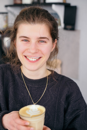 Smiling and positive girl with latte coffee foam on the lipsの写真素材