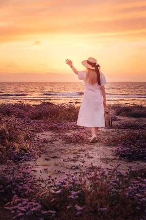 Beautiful blonde woman in white dress travel to Cyprus and enjoying summer sea sunset near the lighthouse beach, back view. Freedom conceptの写真素材