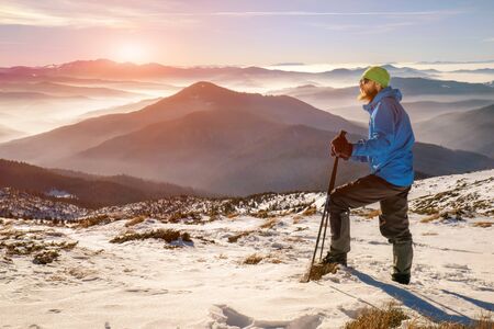 Man hiker stand with trekking sticks on the mountain summit over the clouds and enjoying beautiful winter landscape.の写真素材