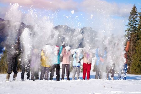 Group of happy friends have fun and throwing snow in the air in winter mountains at sunny day
