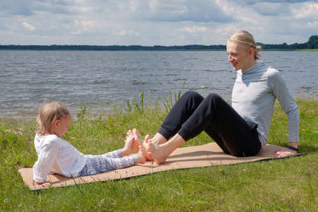 Father play with child and doing yoga exercise outdoors near the lakeの写真素材
