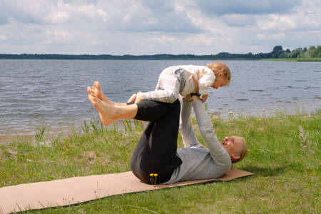 Father play with child and doing yoga exercise outdoors near the lakeの写真素材
