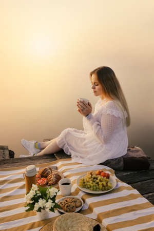 Woman with coffee cup on picnic near foggy lake at sunriseの写真素材